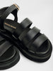 Black sandals with three padded leather straps, a chunky platform sole, and gold ankle buckle shown in a close-up side angle.