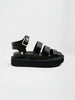 Black leather sandals with three padded straps, a gold ankle buckle, and a chunky platform sole shown in a full side profile.