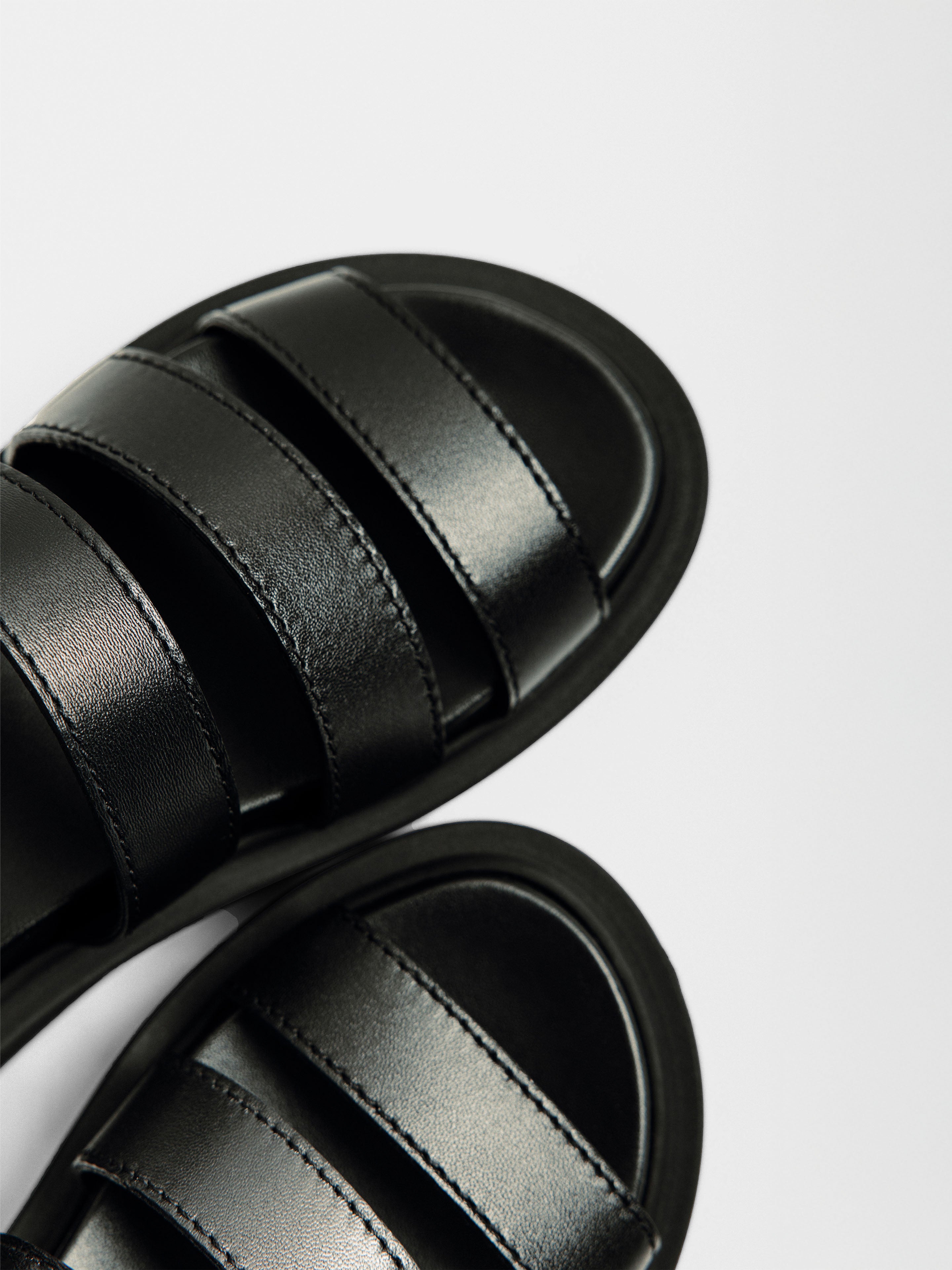 Leather sandals in black with three padded straps, topstitched detailing, and a chunky rounded platform sole shown in a close-up overhead angle.
