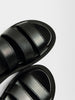 Leather sandals in black with three padded straps, topstitched detailing, and a chunky rounded platform sole shown in a close-up overhead angle.