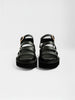 Casual black sandals with three horizontal leather straps, gold buckle ankle closure, and a chunky black platform sole shown front-facing as a pair.