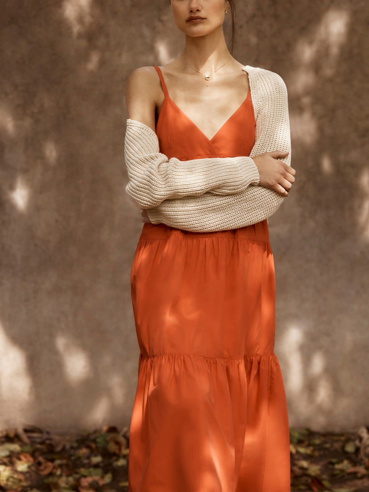 Woman wearing a burnt orange satin Serra dress with a cream cardigan tied at the waist