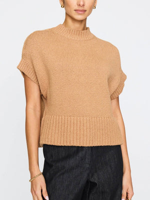 Sleeveless women's sweater in camel with ribbed hem and wide neckline styled with dark denim trousers.