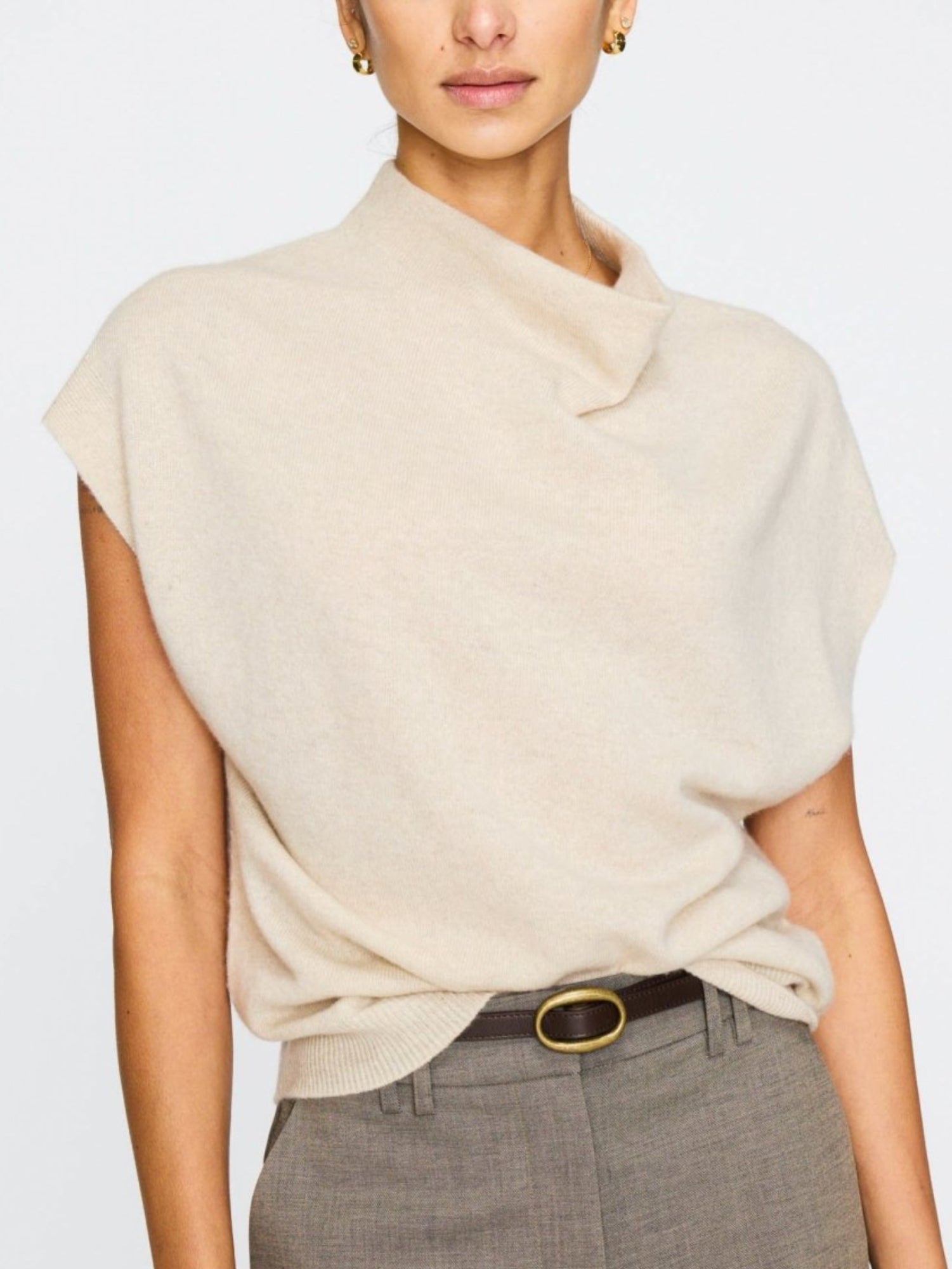 Cashmere top for women with a slightly asymmetric neckline and capped sleeves, tucked into high-waisted grey trousers with a belt.
