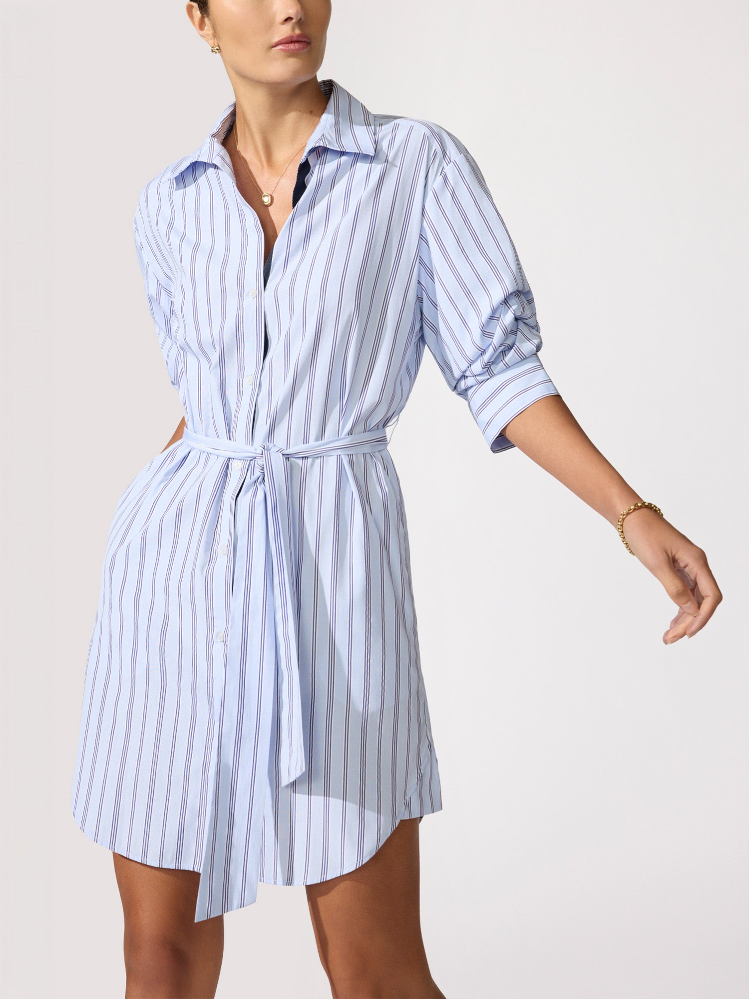 Woman wearing a blue and white striped shirt dress with rolled sleeves and a tie-waist belt.