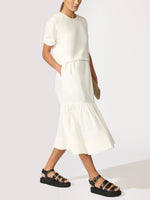 Woman wearing an ivory cropped top and tiered midi skirt set with black strappy platform sandals.