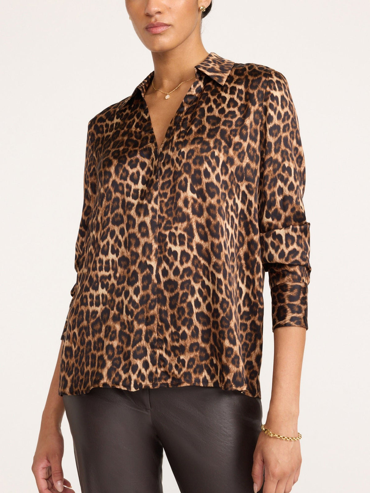 Woman wearing a women's leopard print button-up blouse with rolled sleeves and a gold bracelet, paired with black leather pants