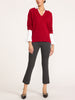 Woman wearing a women's red v-neck sweater layered over a white long-sleeve blouse, with dark gray cropped pants and black pointed flats