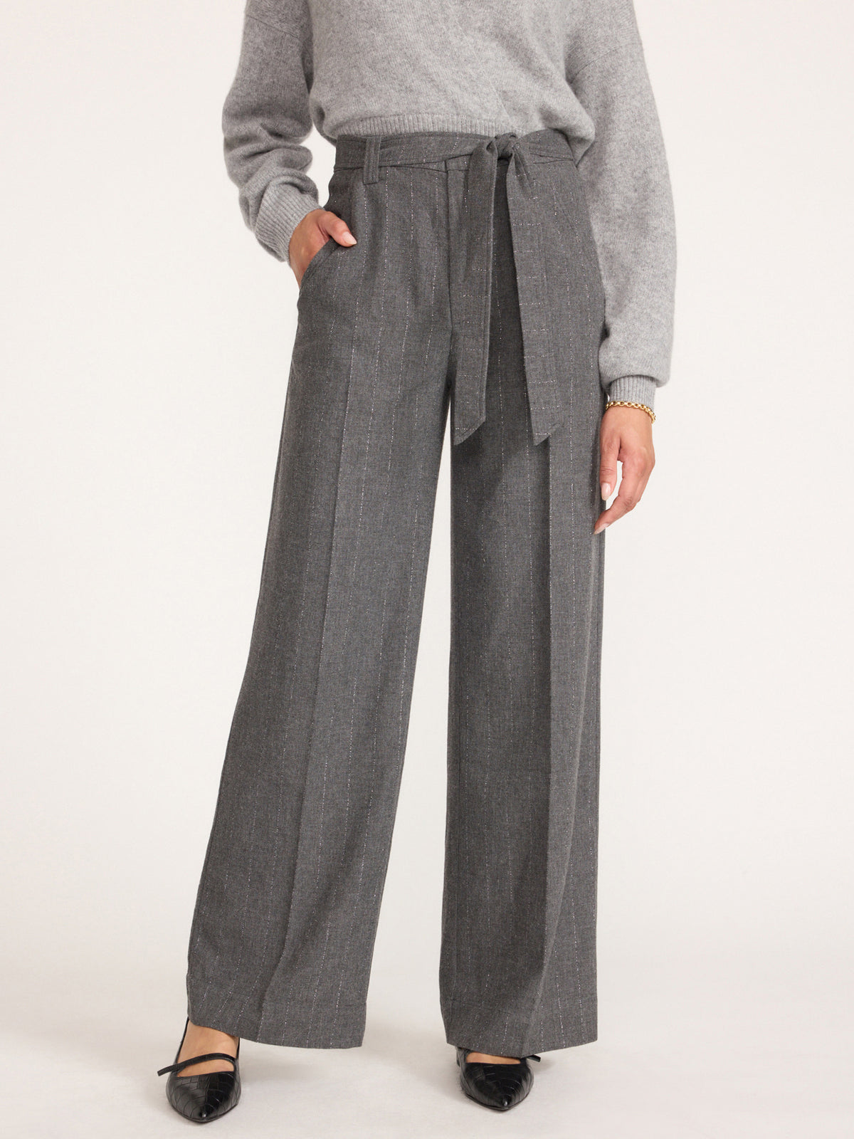 Front view of a woman wearing women's gray flannel wide-leg trousers with a fabric tie belt, gray sweater and black pointed flats