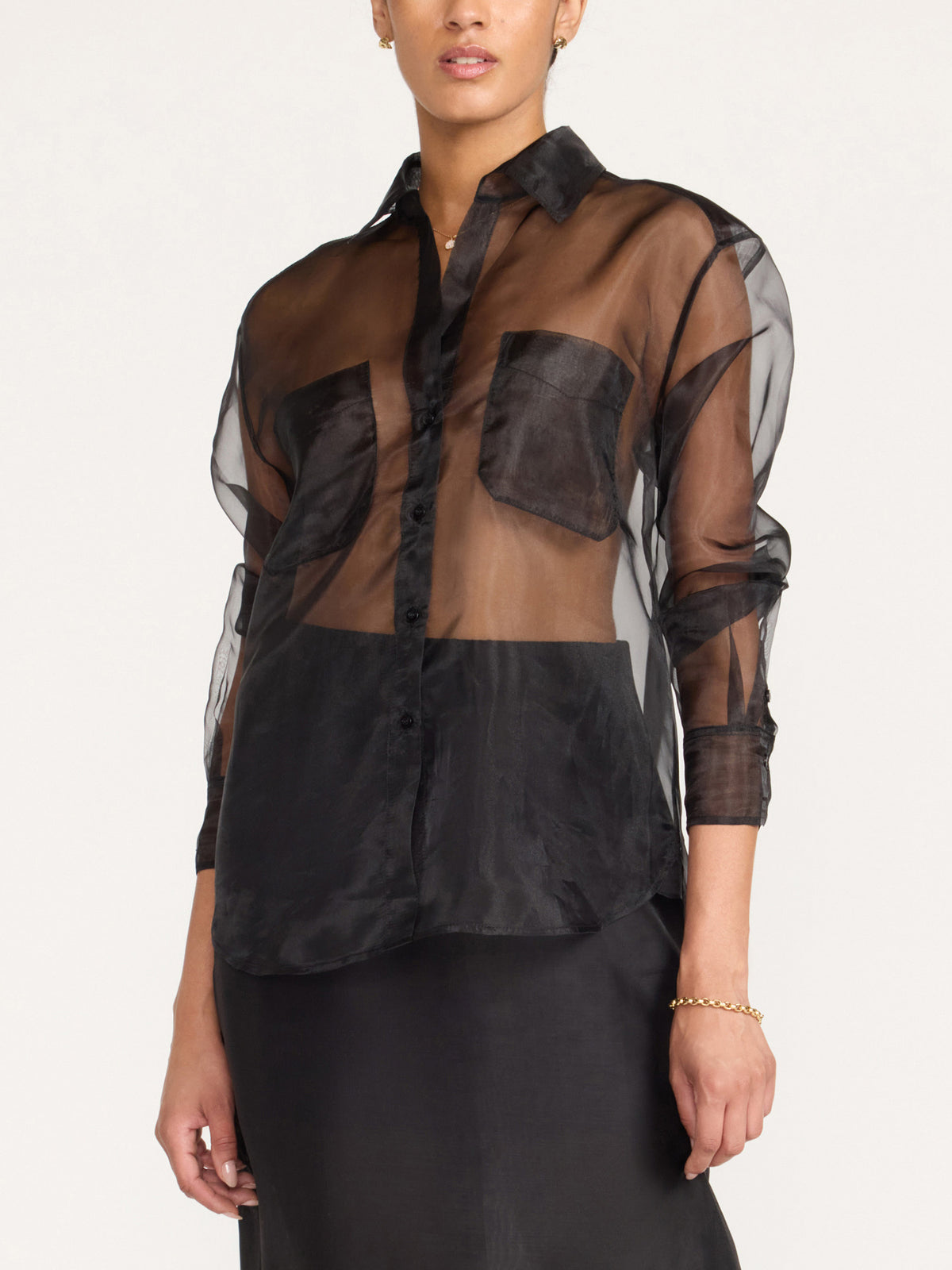 Close-up of a woman wearing a women's sheer black button-up shirt with patch pockets over a black skirt