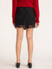 Back view of a woman wearing a women's black lace mini skirt with a scalloped hem, red sweater and black flats