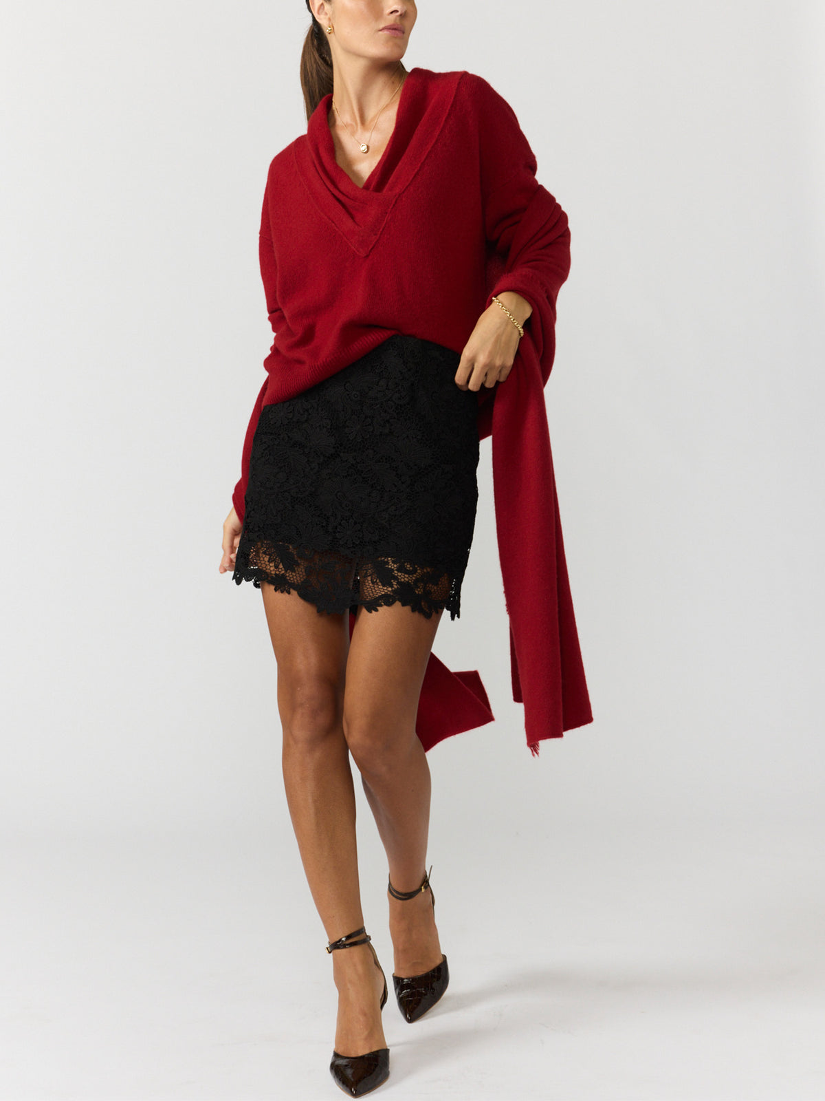 Women's red wrap sweater with a V-neck and long draped panel, styled with a black lace mini skirt and ankle-strap heels