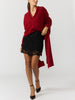Women's red wrap sweater with a V-neck and long draped panel, styled with a black lace mini skirt and ankle-strap heels