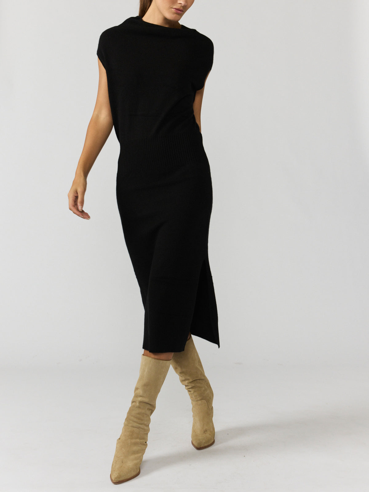 Women's black sleeveless midi dress with a funnel neck and side slit, styled with tan suede boots