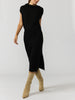 Women's black sleeveless midi dress with a funnel neck and side slit, styled with tan suede boots