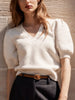 Women's white cotton cardigan with short puff sleeves styled with dark trousers and a brown leather belt.
