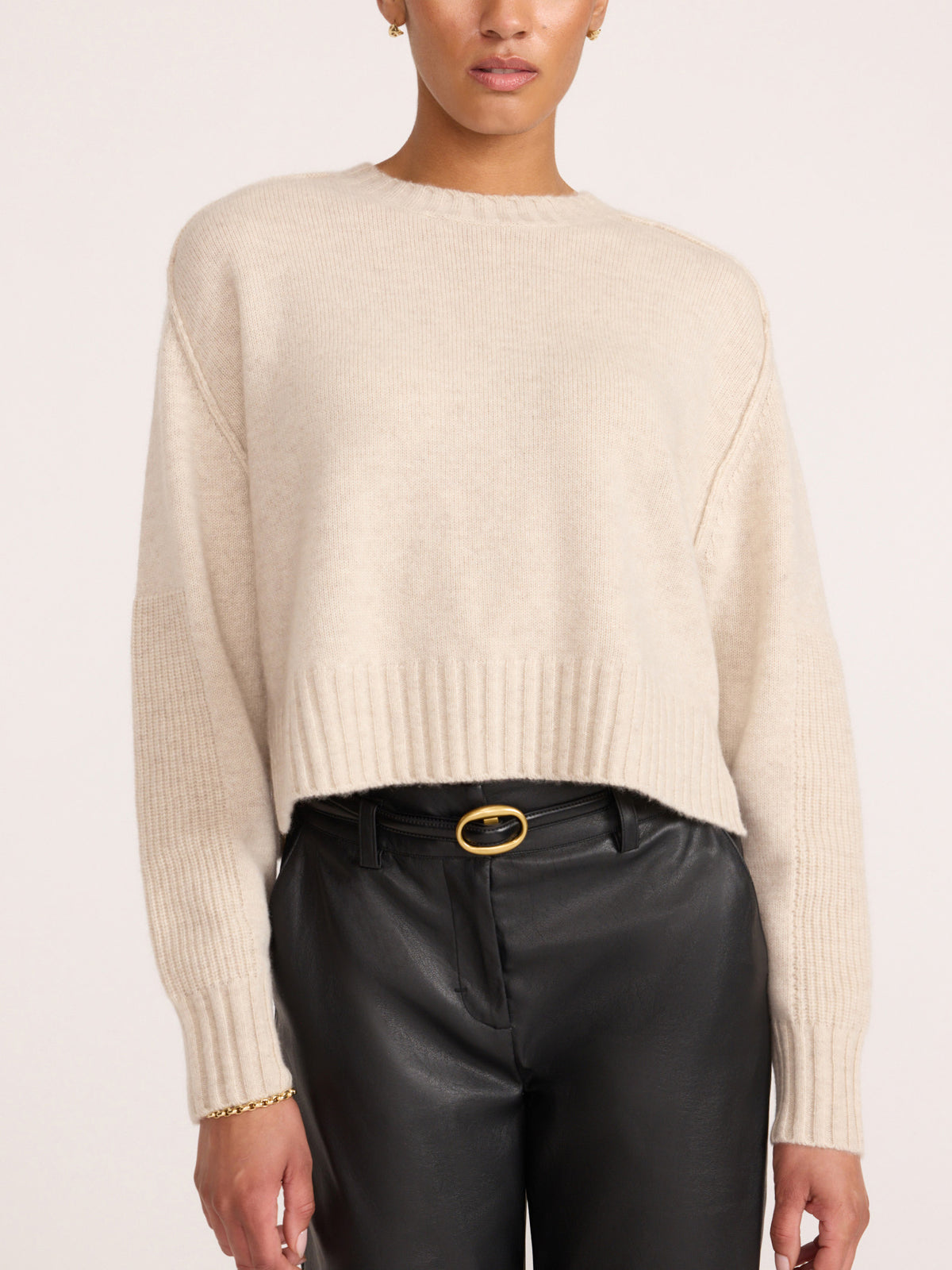 Women's cream cashmere crewneck sweater styled with black leather pants and a gold buckle belt