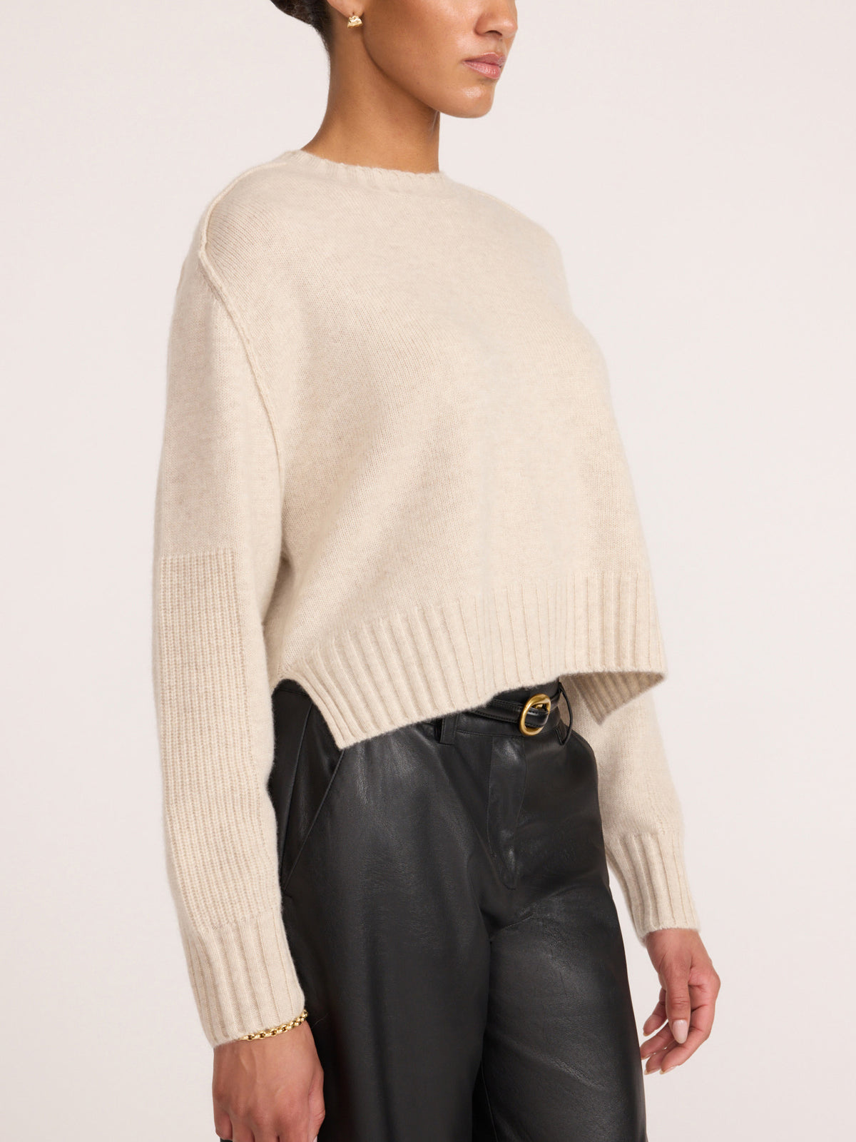 Side profile of a women's cropped cream cashmere crewneck sweater with ribbed hem, paired with black leather pants
