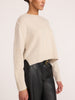 Side profile of a women's cropped cream cashmere crewneck sweater with ribbed hem, paired with black leather pants