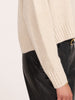Close-up of a women's cream cashmere crewneck sweater with ribbed cuffs, paired with black leather pants