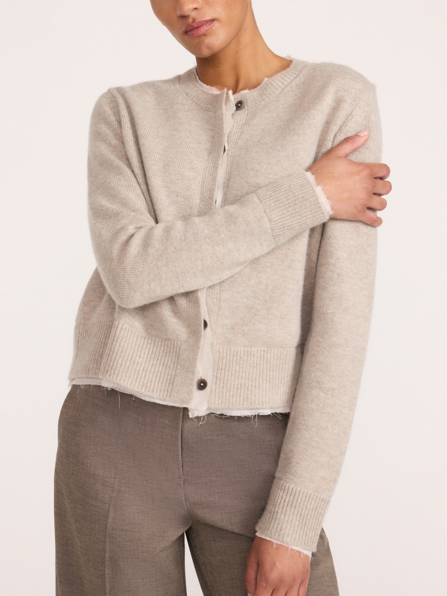 Close-up of a woman wearing the Brochu Walker Archie Layered Cardigan in Gravel Stone Melange, a buttoned knit cardigan with a raw hem, paired with taupe trousers.
