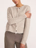 Close-up of a woman wearing the Brochu Walker Archie Layered Cardigan in Gravel Stone Melange, a buttoned knit cardigan with a raw hem, paired with taupe trousers.