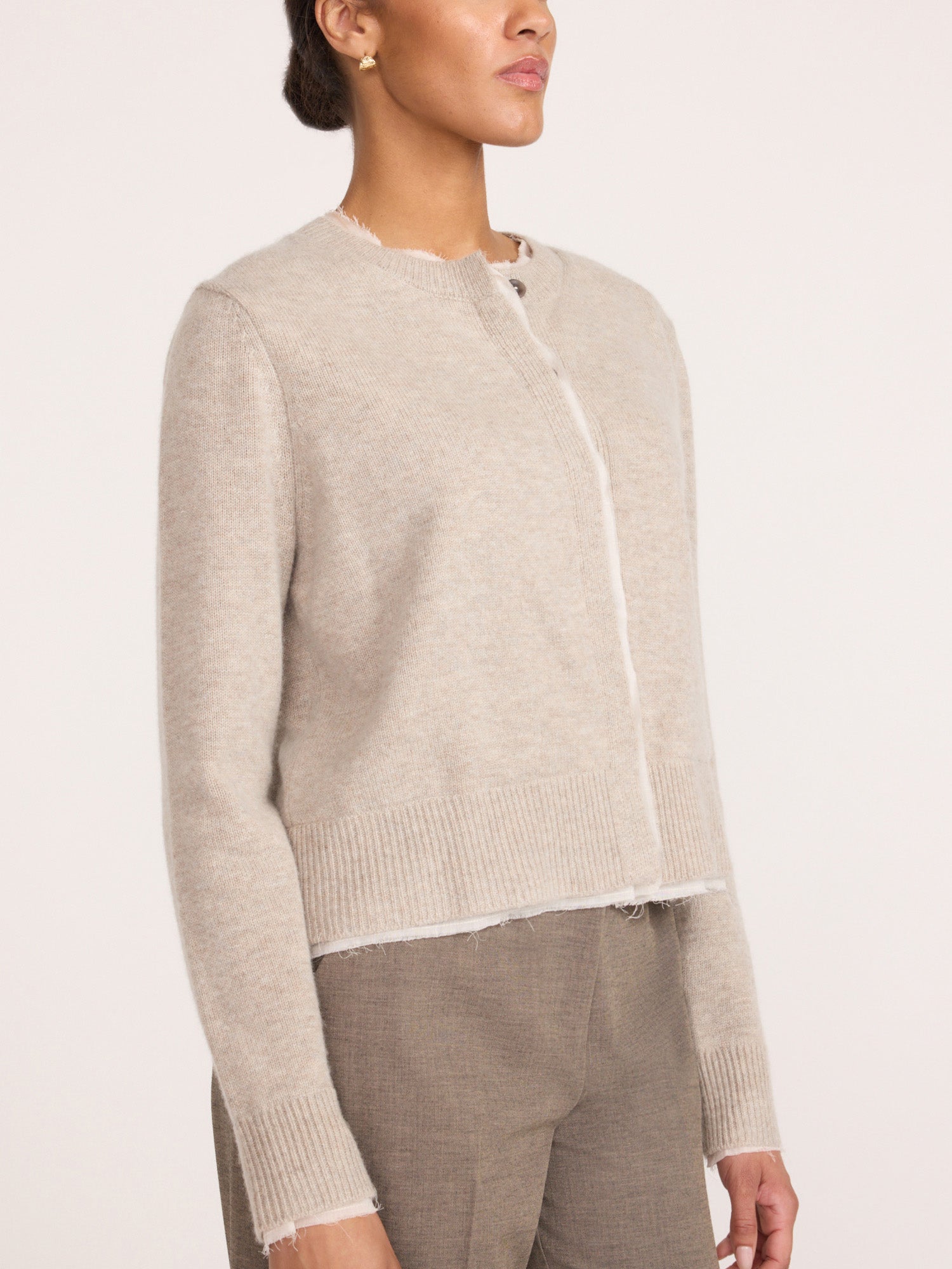 Woman wearing the Brochu Walker Archie Layered Cardigan in Gravel Stone Melange, a cropped knit cardigan with raw frayed edges, paired with taupe trousers.
