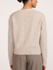 Back view of a woman wearing the Brochu Walker Archie Layered Cardigan in Gravel Stone Melange, a light beige knit sweater with a center seam, paired with taupe trousers.