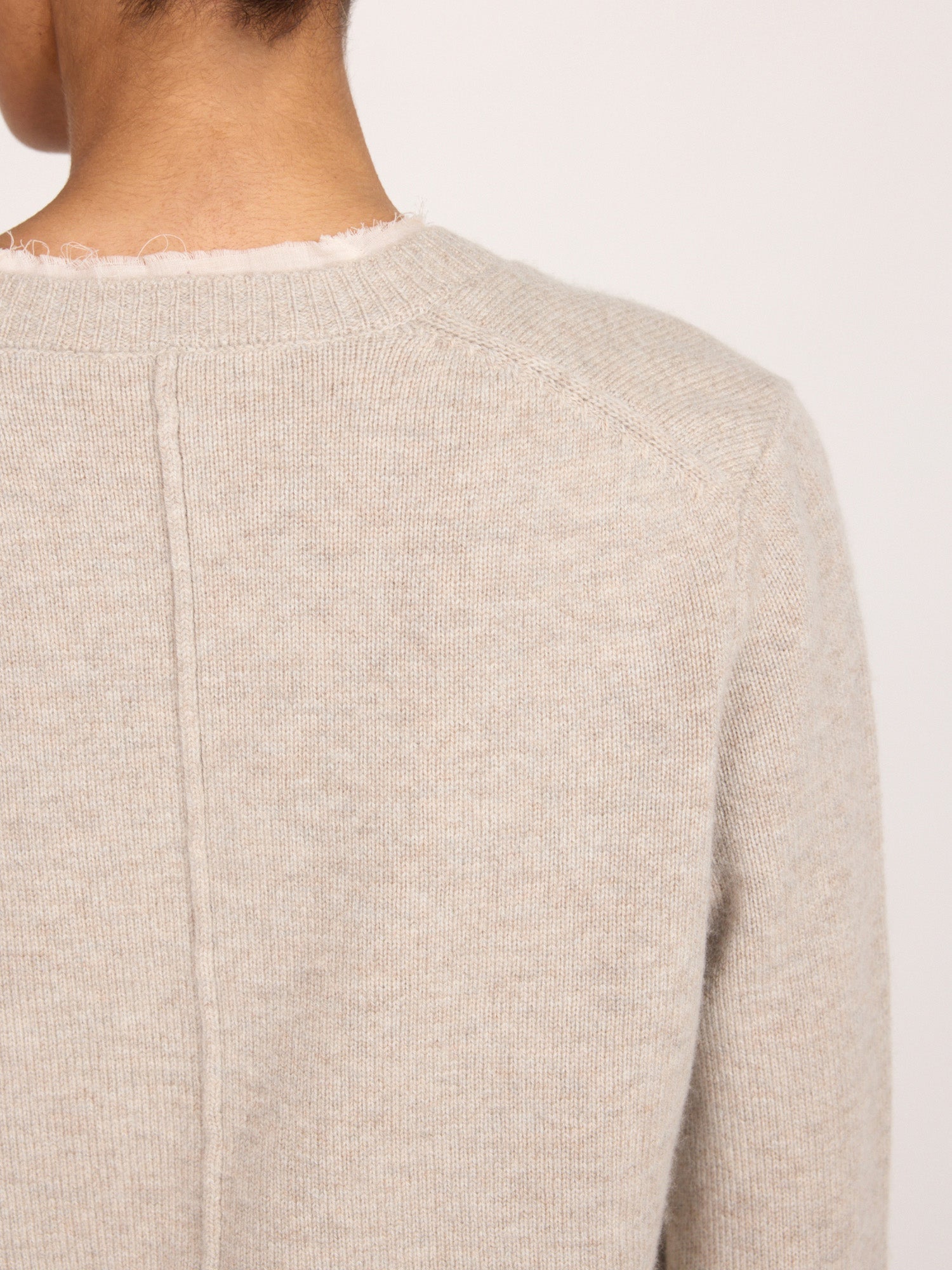 Close-up back view of the Brochu Walker Archie Layered Cardigan in Gravel Stone Melange, a light beige knit sweater showing the raw-edge neckline.