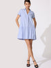 Striped mini dress in blue and white pinstripe with cap sleeves, a drop-waist tiered skirt, V-neckline, and side pockets worn with black heeled sandals.