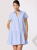 Striped mini dress in blue and white pinstripe with cap sleeves, an open collar, drop-waist ruffle hem, and side pocket shown front-facing.