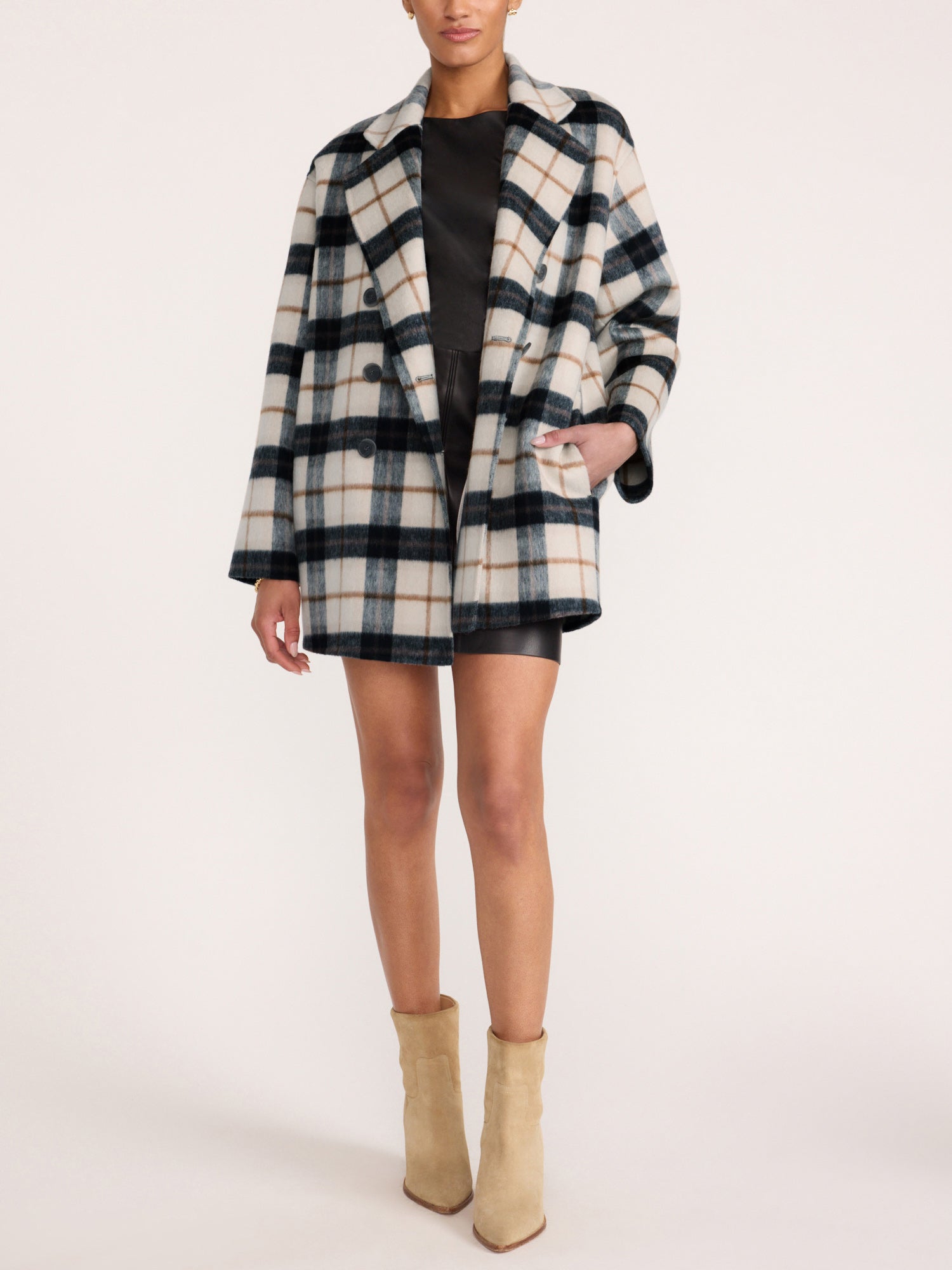 Full-length view of a woman wearing the Brochu Walker Bodhi Double Breasted Plaid Coat in Montclair Plaid over a black mini dress and beige ankle boots.