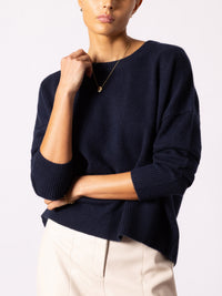 Model wearing navy cashmere crewneck sweater with ribbed cuffs and hem over ivory pants.