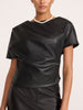 Close-up of a woman wearing the Brochu Walker Cleo Top in Black Onyx, a draped faux-leather top with an asymmetrical neckline, styled with a pearl necklace.