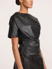 Side view of a woman wearing the Brochu Walker Cleo Top in Black Onyx, a faux-leather top with short puff sleeves, paired with a matching black skirt.