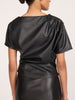 Back view of a woman wearing the Brochu Walker Cleo Top in Black Onyx, a faux-leather top with a draped gathered neckline, paired with a matching black skirt.
