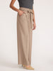 Side view of a woman wearing the Brochu Walker Duke Suit Pant in Tawny, high-waisted wide-leg trousers with a tie belt, styled with a gray top and heels.