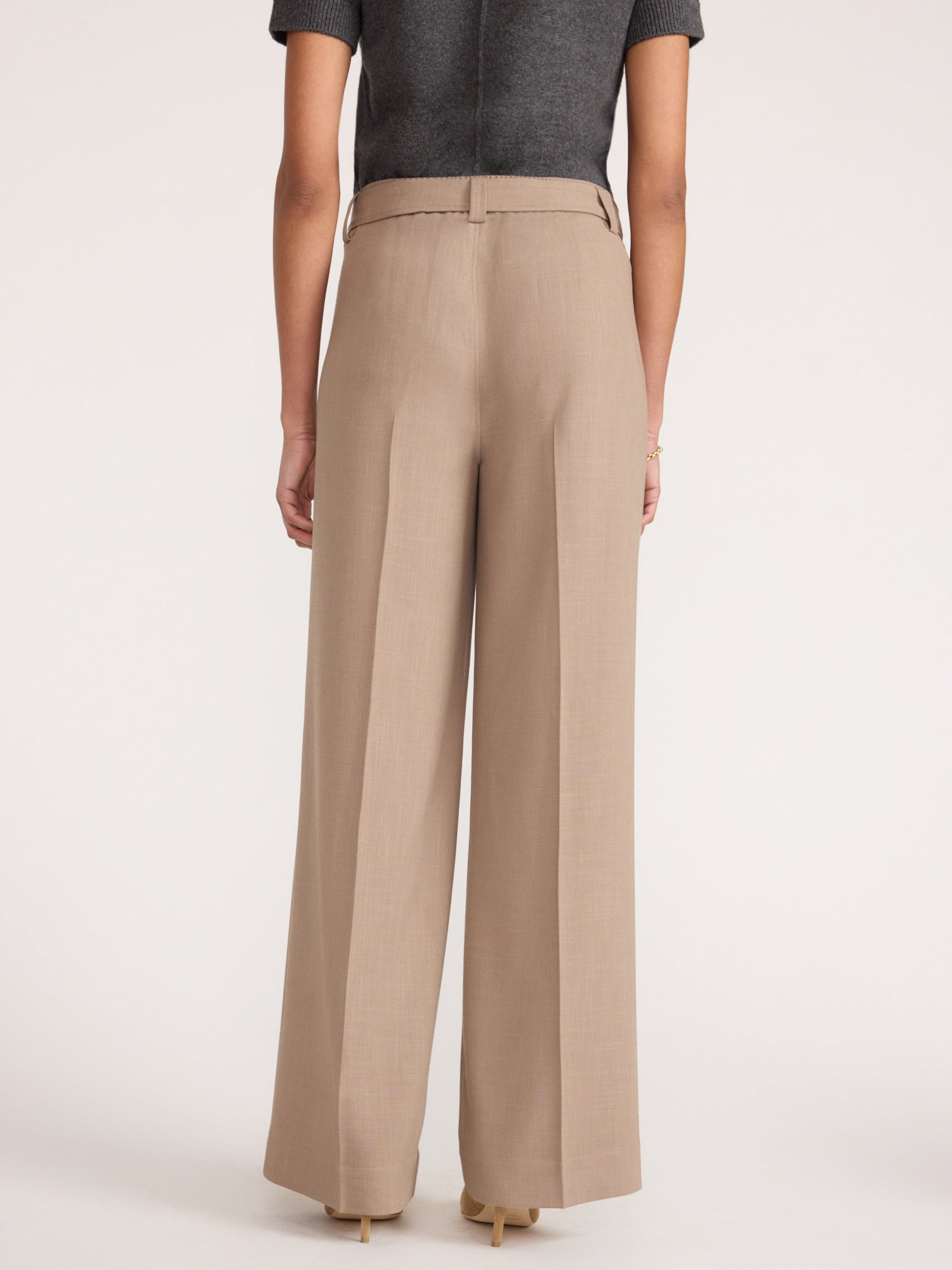 Back view of a woman wearing the Brochu Walker Duke Suit Pant in Tawny, high-waisted wide-leg trousers styled with a gray top and beige heels.