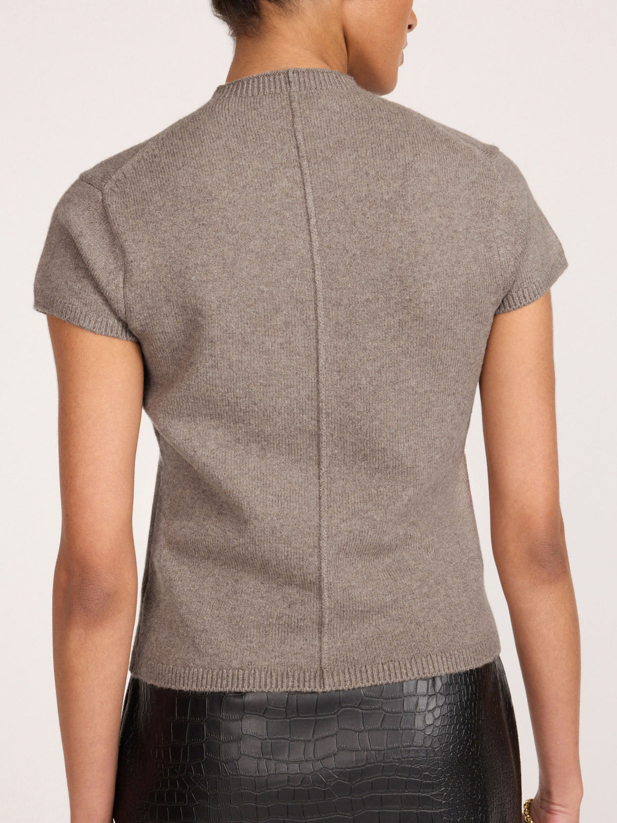 Back view of a woman wearing the Emmy cotton-wool cardigan in otter melange, paired with a black crocodile-embossed skirt.