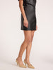 Waist-down view of a woman wearing the Brochu Walker Esme Miniskirt in Black Onyx, a faux-leather mini skirt styled with beige pointed-toe heels.