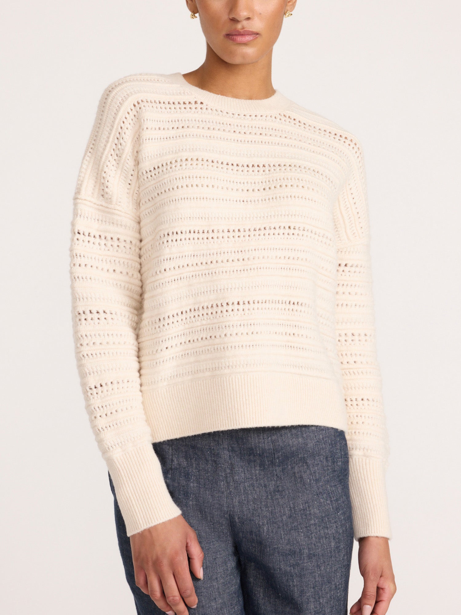 Close-up of a woman wearing the Brochu Walker Everyday Multistitch Bright Crew sweater in Oatmeal Melange, a cream open-knit crewneck sweater with blue jeans.