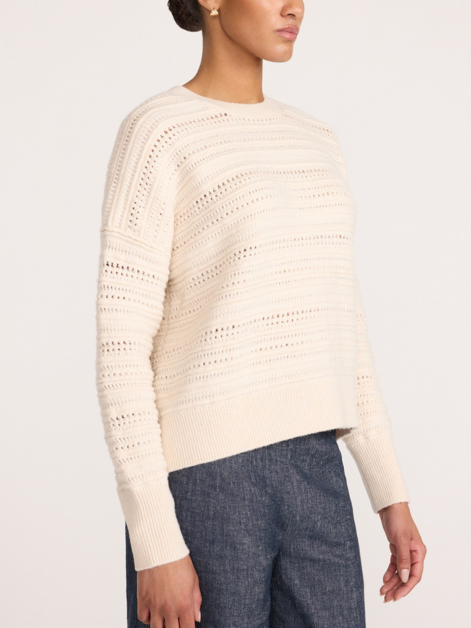 Side profile of a woman wearing the Brochu Walker Everyday Multistitch Bright Crew sweater in Oatmeal Melange, a textured open-knit crewneck sweater with blue jeans.