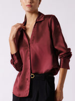 Close-up of a burgundy satin button-down blouse worn open at the collar