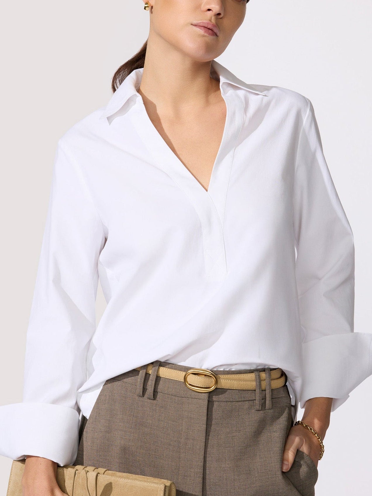 Classy white top in a crisp poplin with a spread collar, V-neckline, and long cuffed sleeves tucked into taupe trousers with a tan oval-buckle belt.
