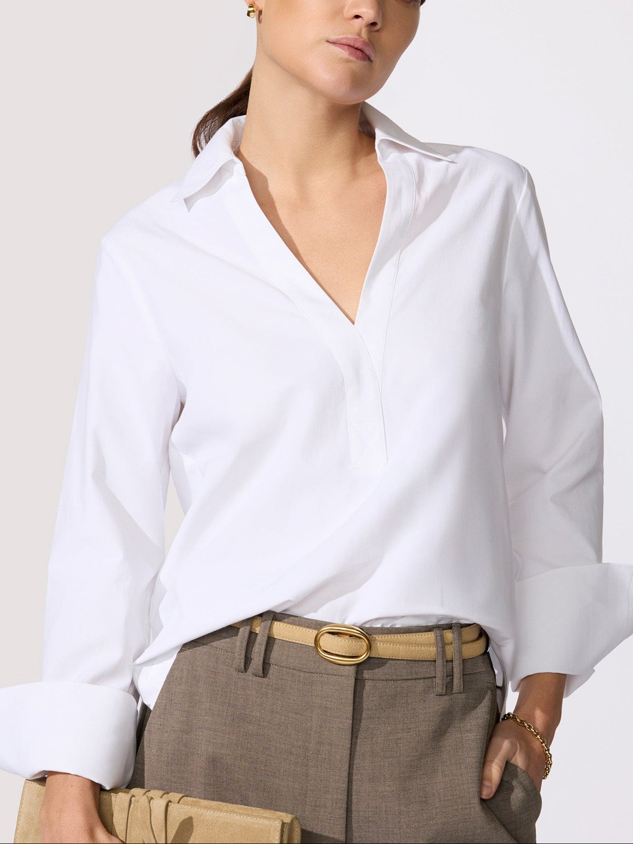Classy white top in a crisp poplin with a spread collar, V-neckline, and long cuffed sleeves tucked into taupe trousers with a tan oval-buckle belt.