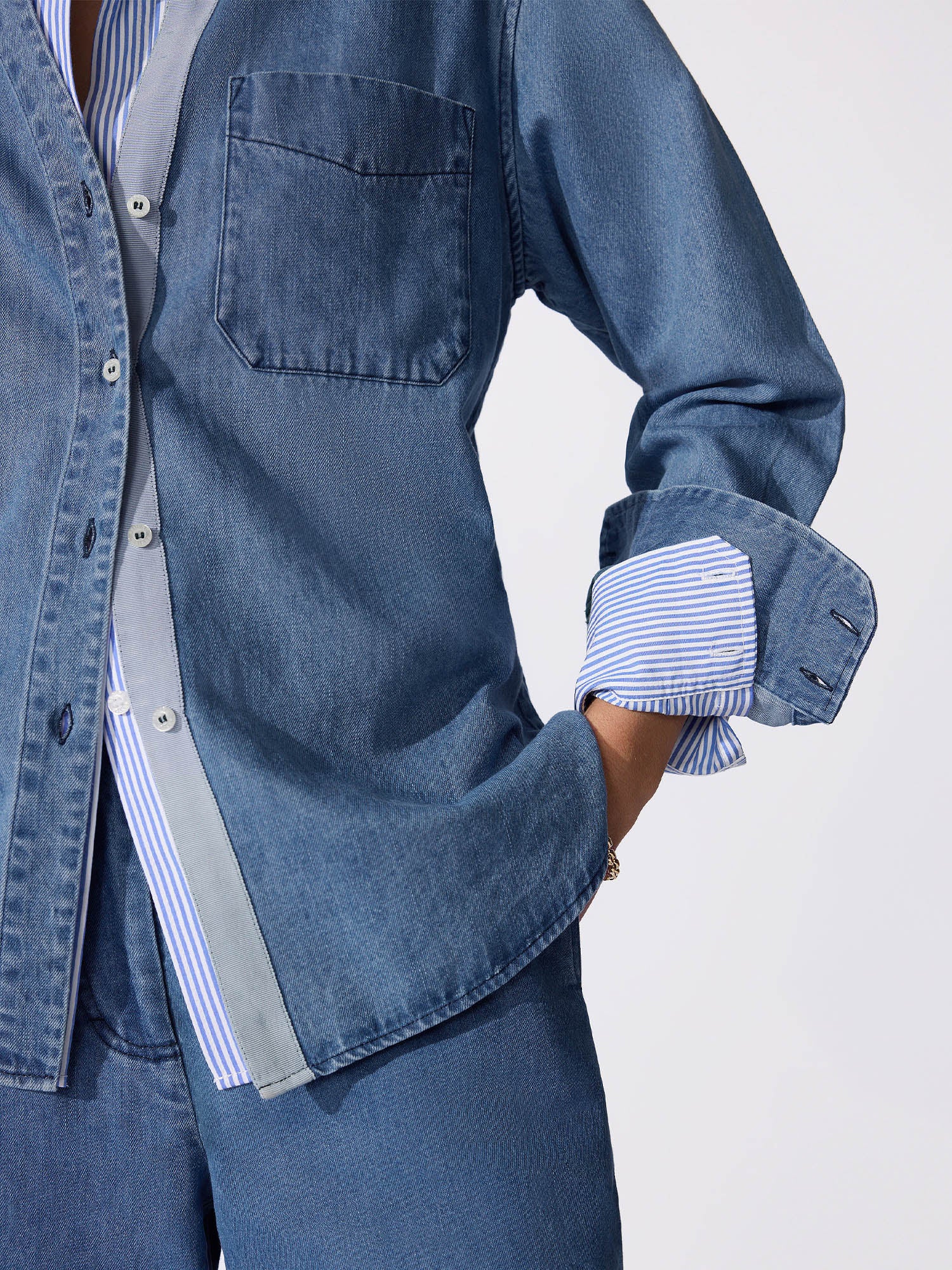 Classy casual clothes featuring a denim overshirt with a striped shirt layered underneath and rolled striped cuffs in close-up.