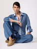 Classy denim outfit in a medium-wash overshirt and wide-leg trousers layered over a striped shirt worn seated on the floor.