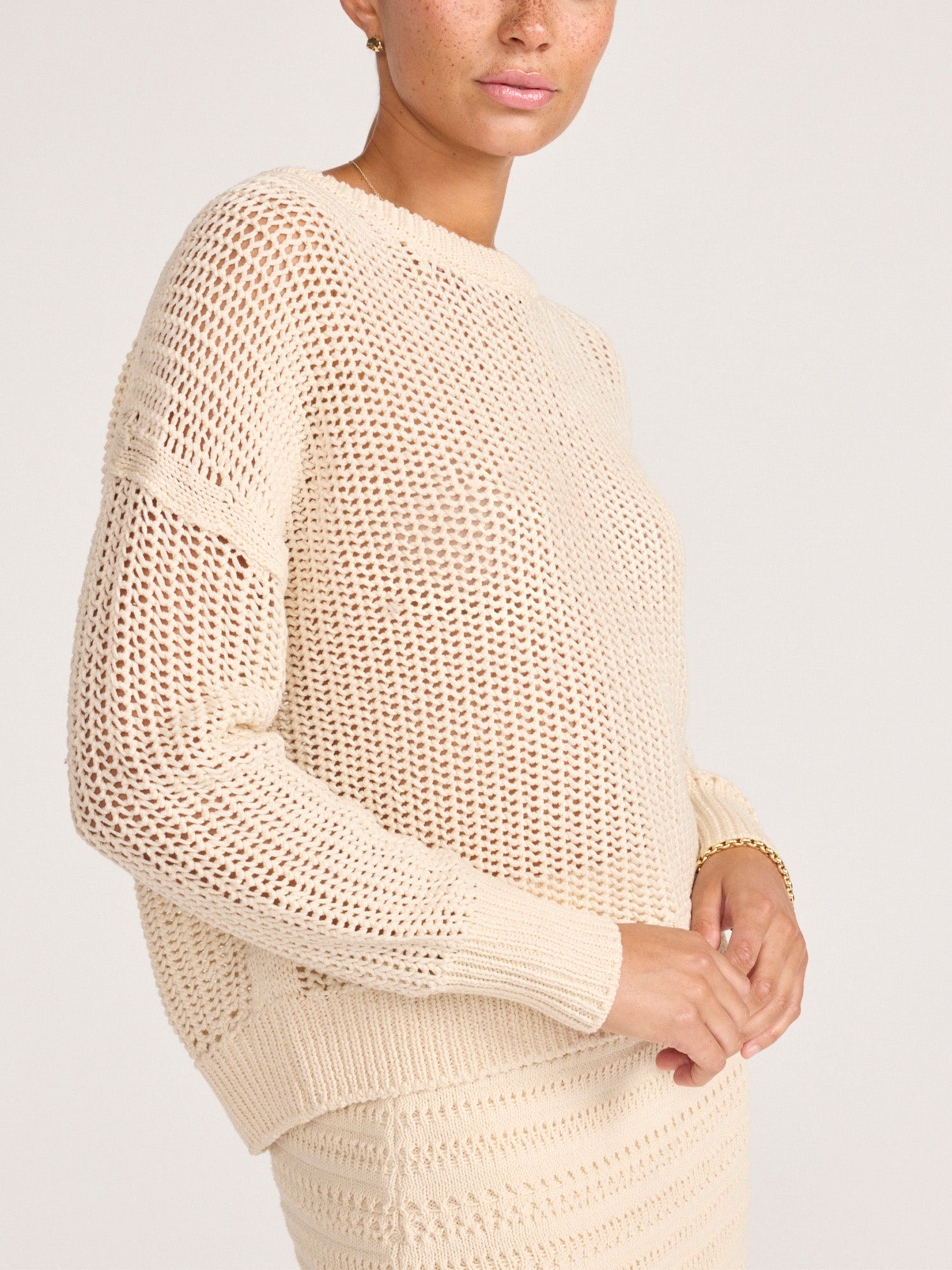 Side view of the ecru open-knit pointelle crewneck sweater, showing the airy stitch pattern and dropped shoulder.