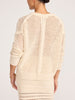 Back view of a model in the ecru Everyday Pointelle Bright Crew, an open-knit women's designer sweater, styled with a textured knit skirt.