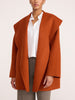 Front view of a woman wearing the Brochu Walker Finley Coat in Canyon Orange, an oversized open-front wool coat over a white shirt and gray trousers.